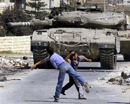 Palestinian children throw stones at Israeli tanks in the West Bank town of Jenin 24 September 2003. Sharon said today any prisoner exchange with the Lebanese Shiite Muslim Hezbollah militia would need cabinet approval and ruled out West Bank Fatah leader Marwan Barghuti's release. AFP PHOTO/SAIF DAHLAH (Photo credit should read SAIF DAHLAH/AFP/Getty Images)